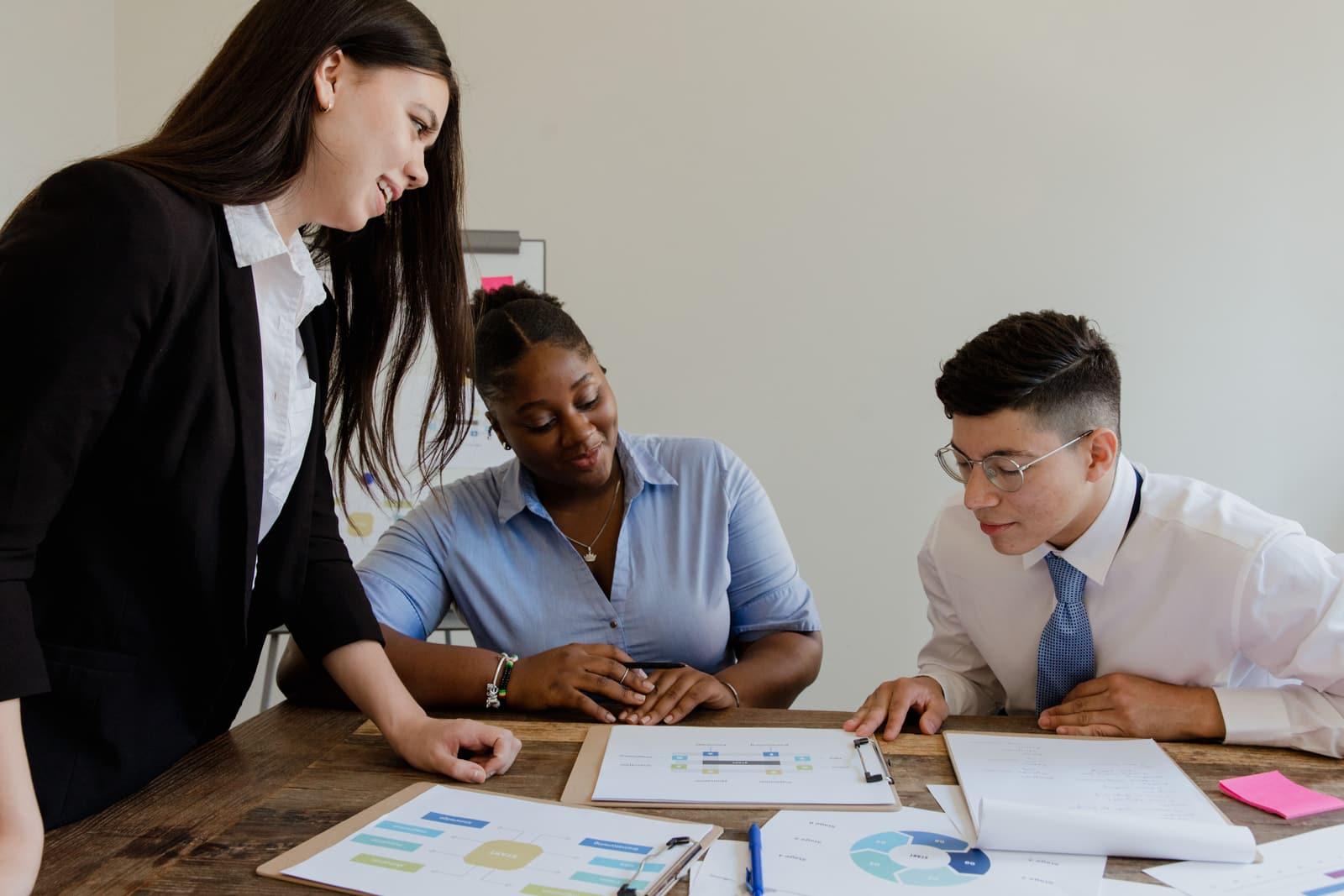 Three colleagues reviewing printed process charts together at a meeting table